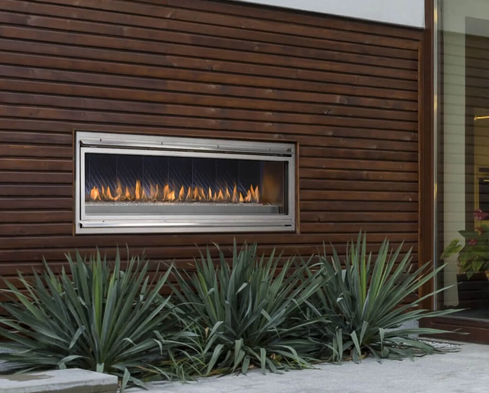 A Montigo Mahana linear outdoor gas fireplace burning in a dark wood-slat patio wall