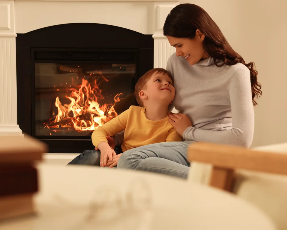 A mother and son together beside a glowing fireplace on a winter evening