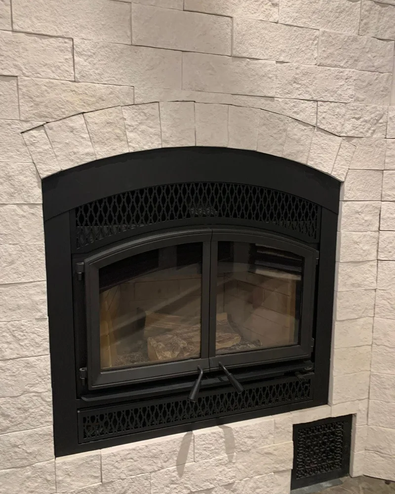 A gas fireplace with a black arched front installed in a white stone surround, from our project gallery