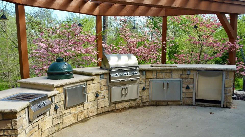 An outdoor kitchen under a pergola with a built-in grill and a Big Green Egg, from our project gallery