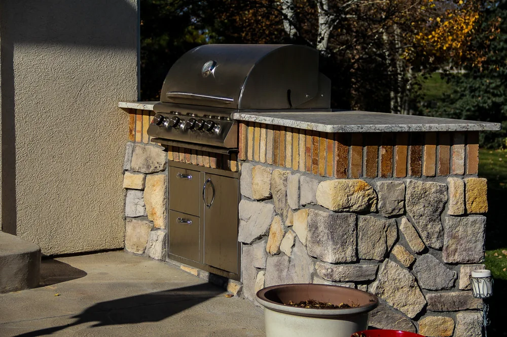 A stone outdoor kitchen with a built-in grill at golden hour, from our project gallery
